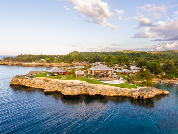 Prise de vue par drone d'un domaine côtier avec des villas modernes, une piscine et des espaces extérieurs gazonnés surplombant l'océan dans un cadre pittoresque.