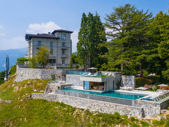 Une photo aérienne d'une propriété de luxe dotée d'une élégante piscine à débordement et d'un salon d'extérieur. Elle est entourée d'une végétation luxuriante, ce qui souligne la proximité du logement avec la nature.
