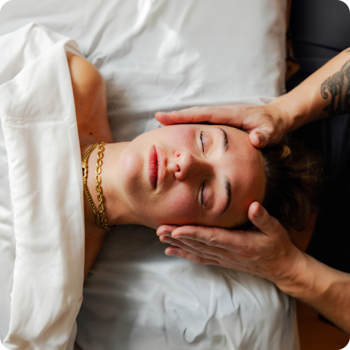 Photo de mains en train de prodiguer délicatement un massage à une personne couverte d'un drap blanc, mettant en avant un service bien-être relaxant.