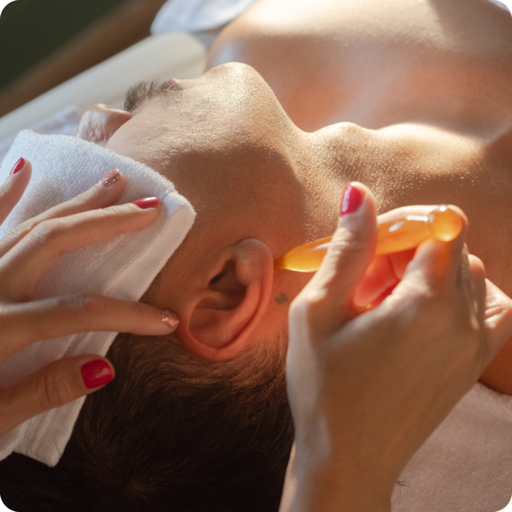 Photo d'une personne se faisant masser le visage à l'aide d'un accessoire en ambre chaud appliqué près de l'oreille, présentant les soins bien-être et spa.