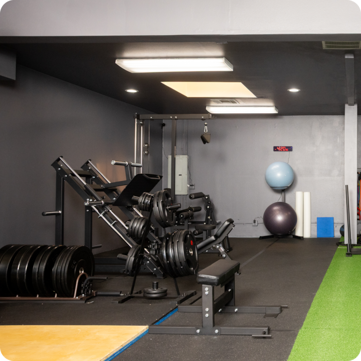 L'intérieur d'un espace de fitness avec des appareils de musculation, des poids empilés, un banc d'entraînement, une surface dédiée à l'entraînement fonctionnel, avec des ballons d'exercice à l'arrière-plan.