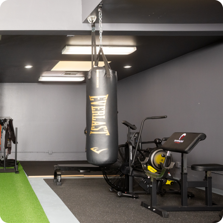 Photo de l'intérieur d'une salle de sport avec un sac de frappe, un vélo d'appartement et un banc de musculation, présentant l'aménagement avant son utilisation.