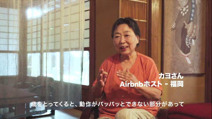 A person sitting in a traditional Japanese-style room with sliding shoji doors and wooden details, wearing an orange shirt. The text on the image reads 'Airbnbホスト - 福岡' and additional text below it in Japanese.