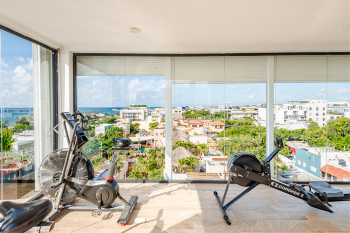 Une salle de sport lumineuse avec vélo et rameur offrant une vue panoramique sur la ville et sur la mer au loin à travers de grandes baies vitrées.