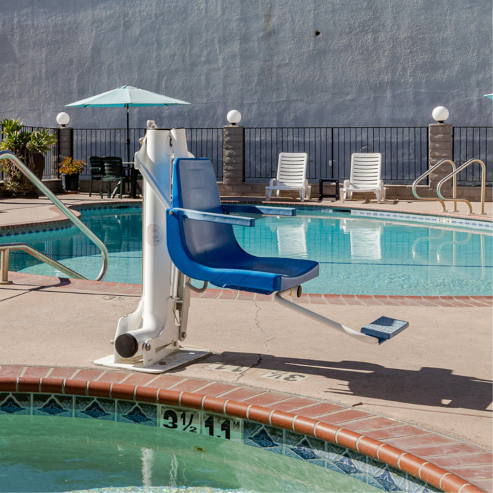 Un lève-personne au bord d'une piscine turquoise, avec des chaises longues et des parasols en arrière-plan sous un ciel ensoleillé.