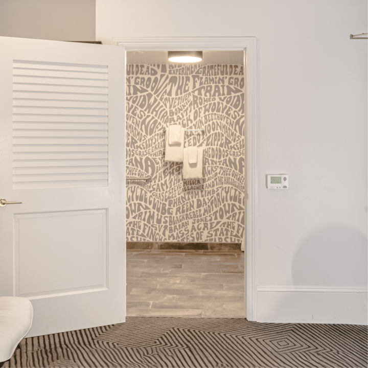 Vue d'une salle de bain à travers une porte ouverte, avec un mur recouvert d'une typographie artistique grise et deux serviettes soigneusement suspendues à un porte-serviettes.