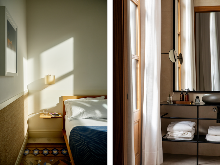 Une chambre d'hôtel élégante baignée par une lumière du jour chaleureuse, dotée d'un lit minimaliste et d'une table de chevet, à côté d'une salle de bain avec des serviettes propres, des articles de toilette élégants et des rideaux fins encadrant une fenêtre en bois et un miroir.