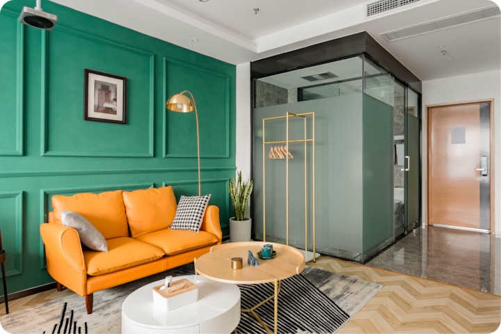 Un studio élégant aux couleurs et aux textures audacieuses, avec un mur vert, un canapé orange, une douche vitrée et un parquet à chevrons.
