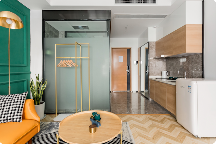 Un studio moderne avec un canapé orange confortable, un lampadaire doré et des détails élégants, notamment un mur vert à moulures et un parquet à chevrons.