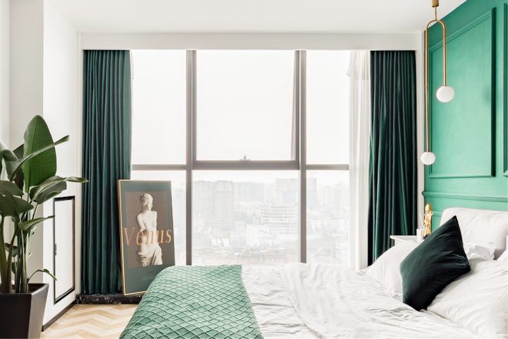 Photo d'une chambre d'hôtel moderne aux tons verts intenses avec une grande fenêtre donnant sur la ville, et mettant en avant un lit accueillant aux draps blancs et verts, une œuvre représentant Vénus et une plante d'intérieur.