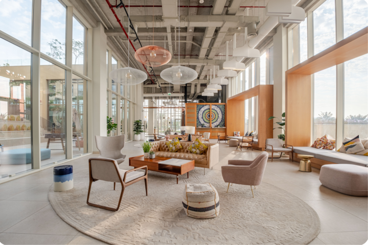Un espace commun élégant dans un hôtel, avec un coin salon accueillant, un tapis texturé, un éclairage artistique et de la lumière naturelle entrant par de grandes baies vitrées.