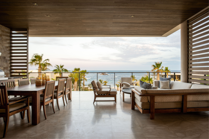 Une terrasse luxueuse offrant une vue panoramique sur l'océan, dotée d'une table à manger, de chaises longues et de plantes tropicales, le tout encadré par des éléments en bois.