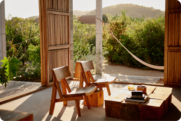 Un espace baigné d'une lumière chaude, avec des meubles en bois et une porte ouverte révélant de la verdure, des collines et un hamac qui se balance dans la douce brise.