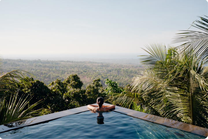 Un cadre paisible avec une piscine à débordement. Une personne profite d'une vue panoramique sur la végétation tropicale et l'océan au loin.