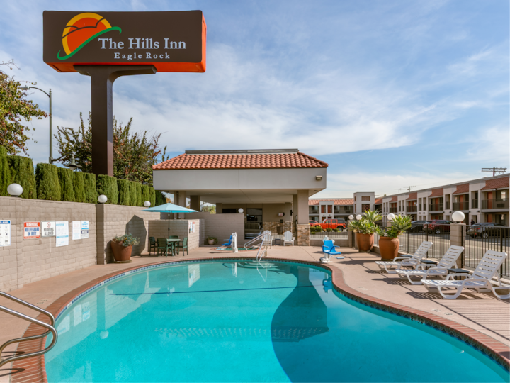 L'enseigne du Hills Inn Eagle Rock surplombant une piscine paisible avec des chaises, des parasols et un cadre paysager par une journée ensoleillée.