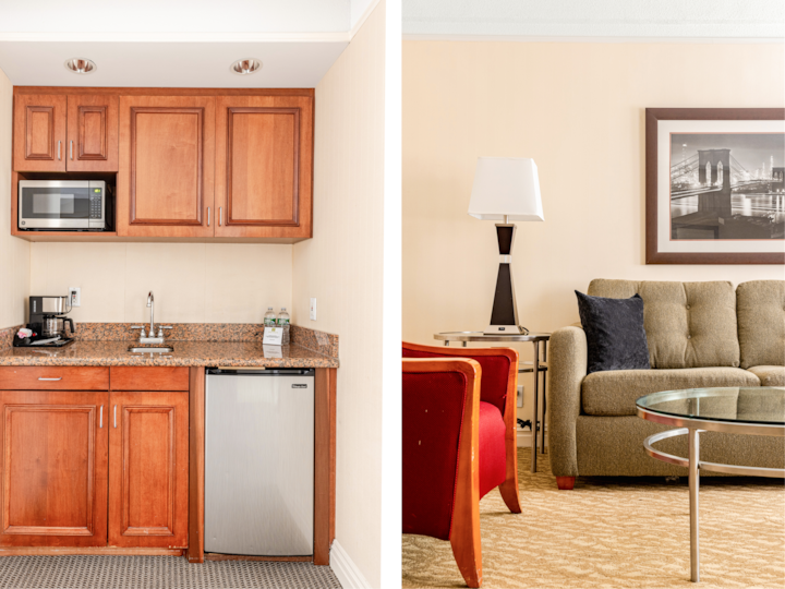 Vue côte à côte d'une kitchenette aux meubles en bois chaleureux et aux appareils électroménagers modernes, et d'un espace de vie équipé d'un élégant canapé aux tons marron, d'un fauteuil rouge, d'une table basse en verre et d'un tableau représentant un pont urbain.