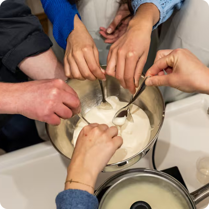 Plusieurs personnes réunies autour d'un bol de cuisine, trempant leur cuillère dans un fromage fondu crémeux.