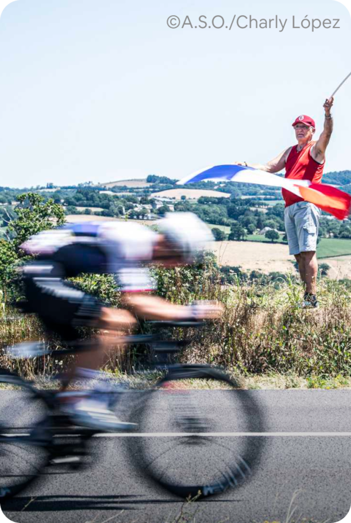 Un cycliste roule sur une route de campagne tandis qu'une personne au bord de la route agite un grand drapeau français. Texte superposé : « Étape 12 – Magny-Cours », avec une flèche vers la droite.