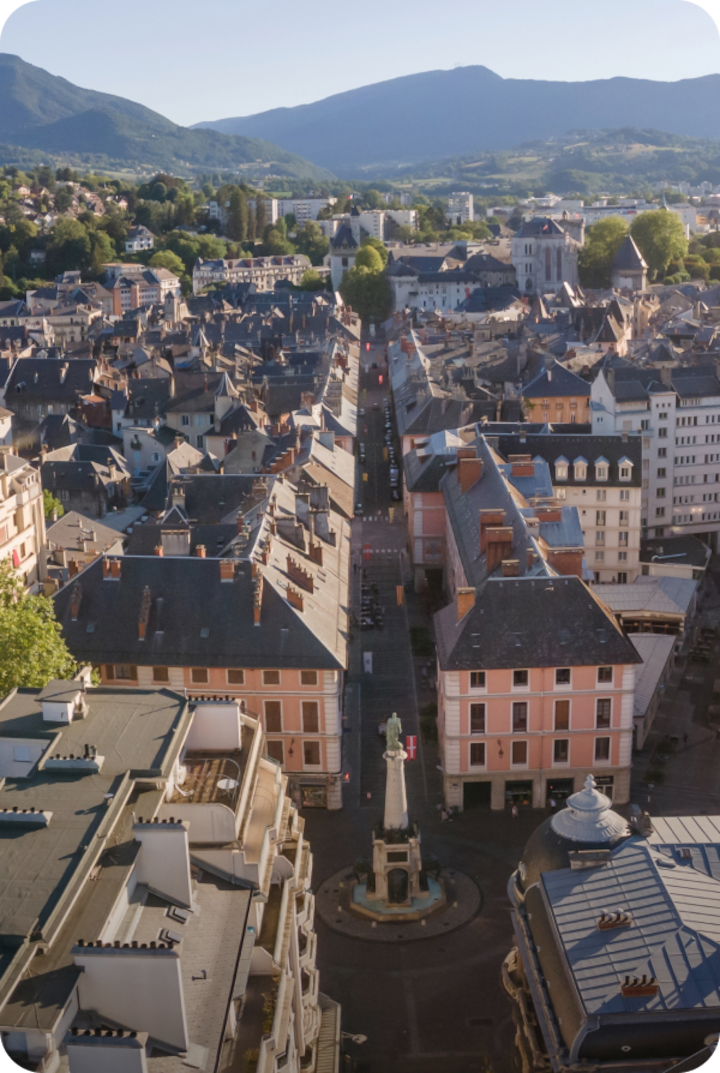 Vue aérienne de Chambéry avec ses toits rapprochés et un mélange d'architecture ancienne et moderne. Texte superposé : « Étape 17 – Chambéry », avec une flèche vers la droite.