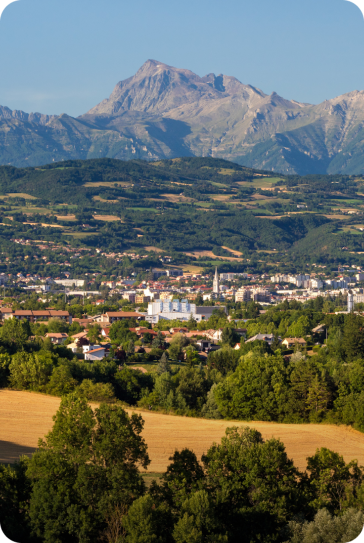 Vue panoramique de Gap entourée de champs et de forêts verdoyantes. Texte superposé : « Étape 19 – Gap », avec une flèche vers la droite.
