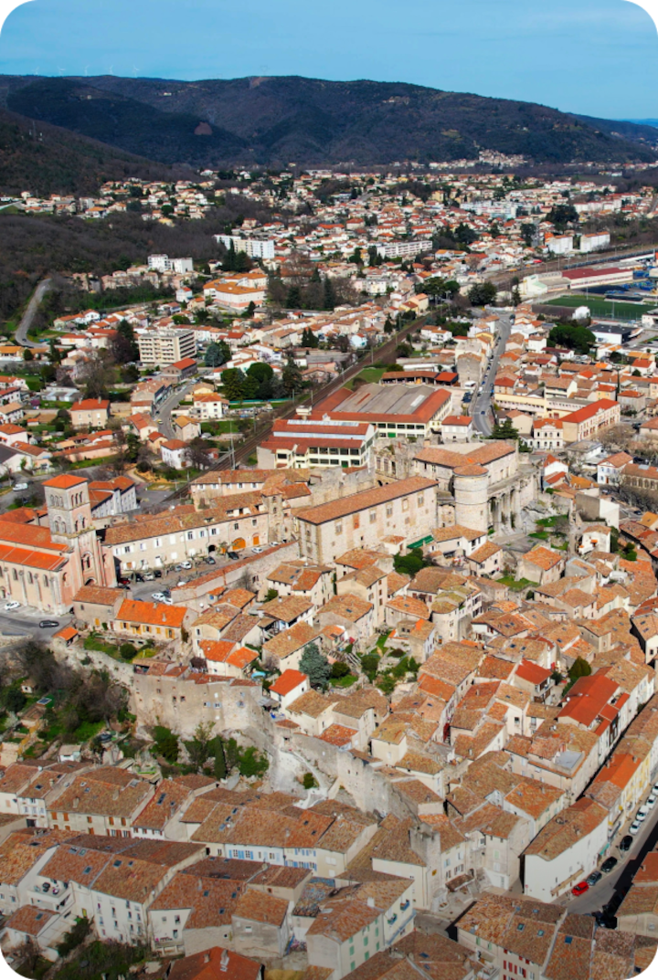 Vue aérienne de La Voulte-sur-Rhône avec ses bâtiments aux toits beiges et orangés. Texte superposé : « Étape 7 – La Voulte-sur-Rhône », avec une flèche vers la droite.