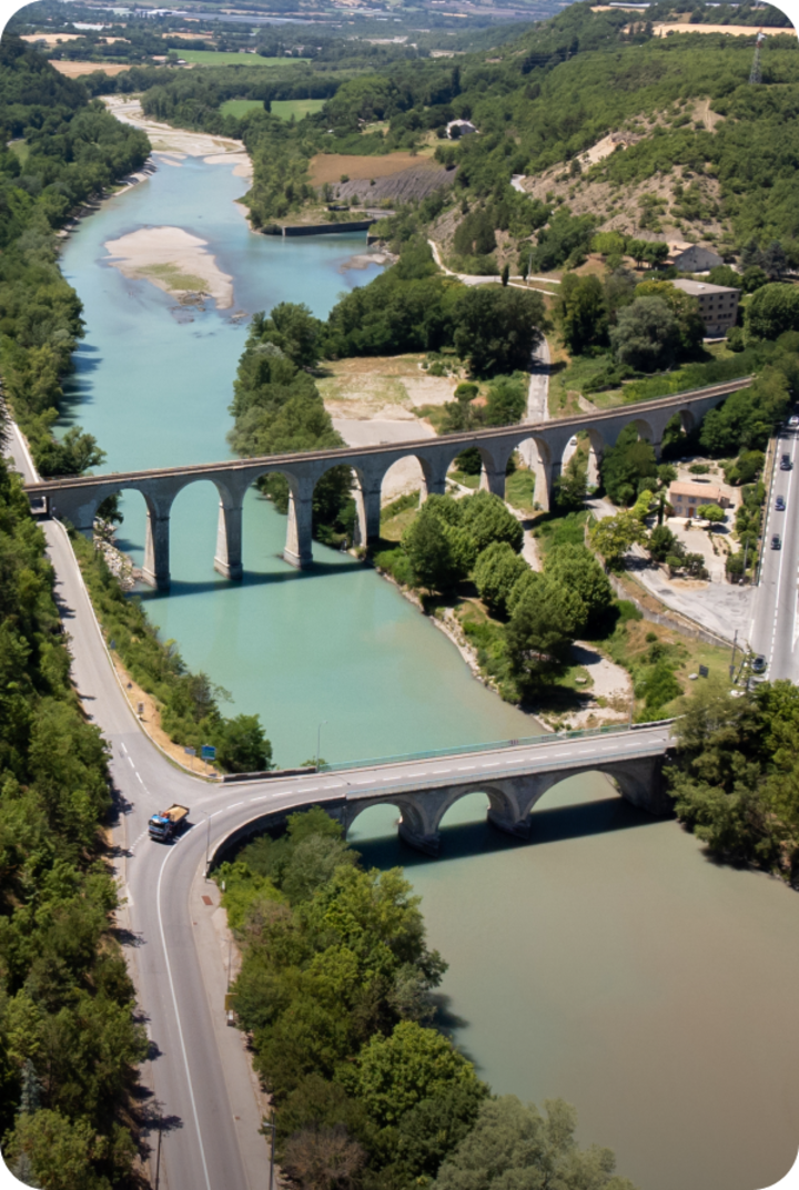 Vue aérienne d'une rivière sinueuse traversée par deux ponts.  Texte superposé : « Étape 8 – Sisteron », avec une flèche vers la droite.