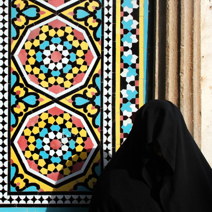 Saudi woman wearing abaya stands in front of mosaic wall