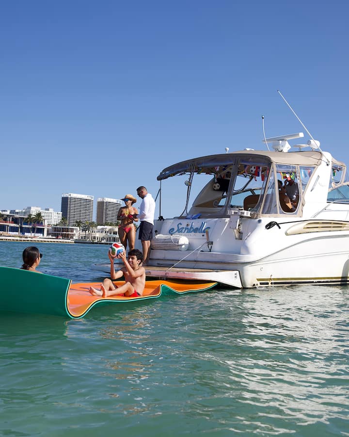 People relax on a giant float off the stern of a charter boat anchored in the water