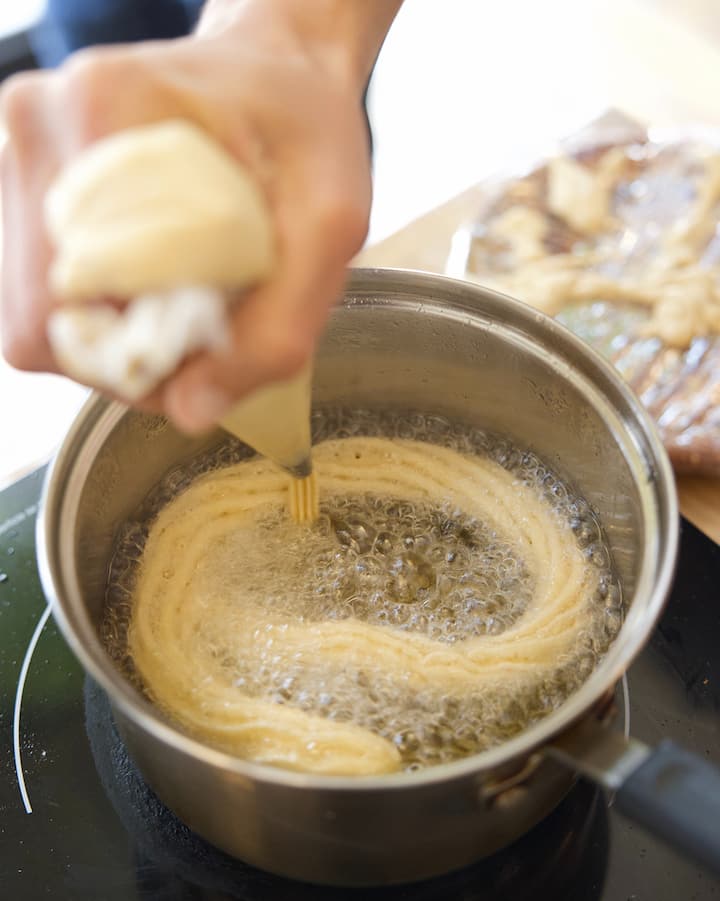 A close up of churro batter being squeezed into a pot of boiling oil