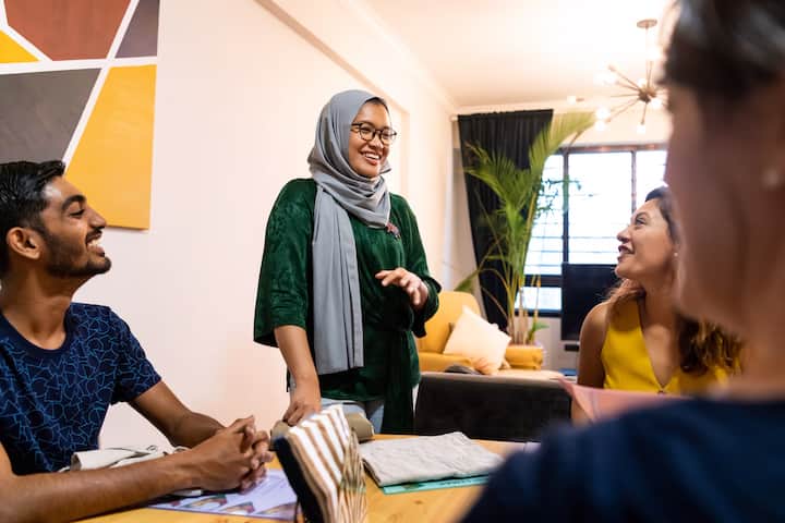 Host in hijab leading a discussion with residents around a table in a Malaysian strata home