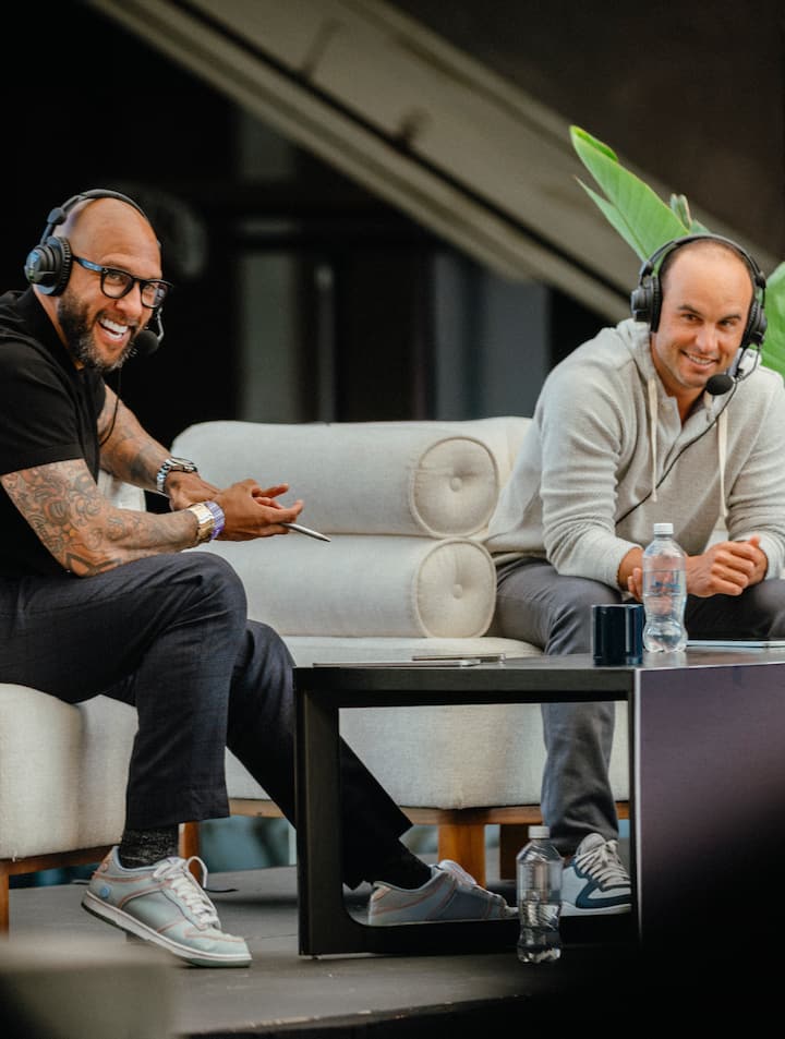 Dos personas con auriculares hablan en un sofá moderno sobre un escenario, lo que indica que se trata de una entrevista para el concepto de un acto de FIFA City.