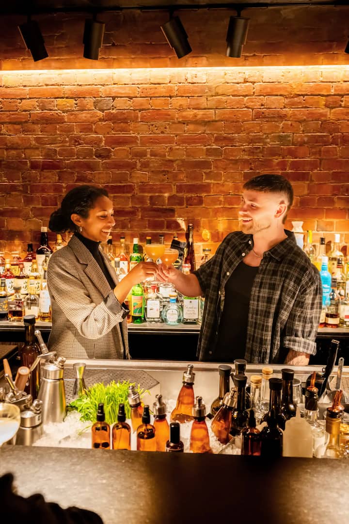 2 people clinking their drinks together behind a bar