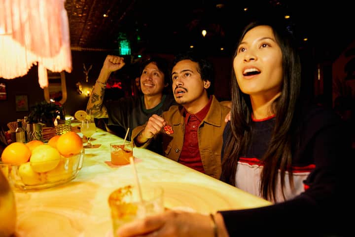 Un grupo de amigos vitorea con bebidas en un animado bar el día de un partido y celebran juntos en la barra.
