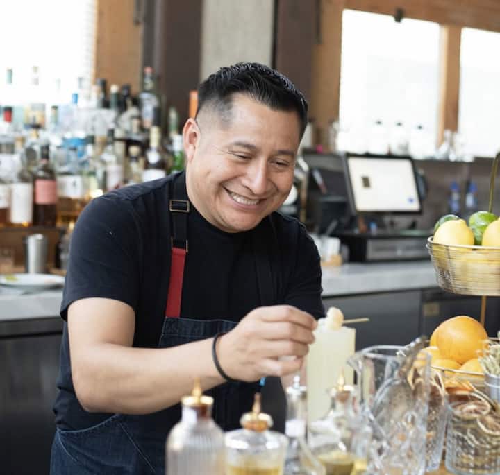 Un barman prepara bebidas en un bar animado y sirve cocteles a aficionados durante un día de partido.