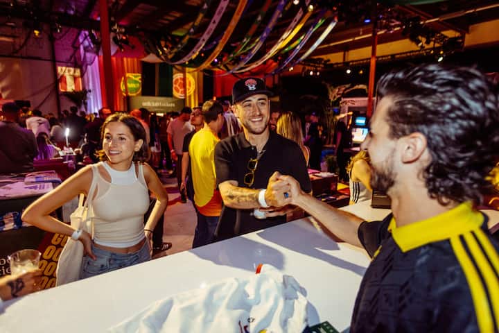 Lors d'un événement animé sur le thème de la FIFA à New York, des supporters discutent près d'un stand de produits dérivés, en dessous de banderoles colorées.