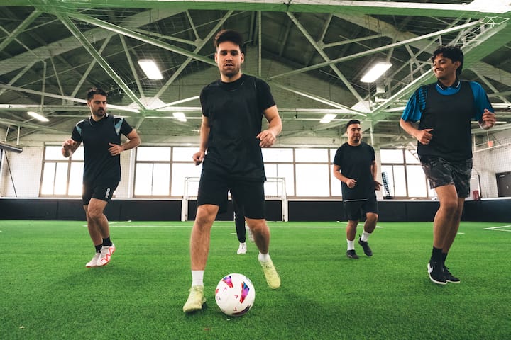 Des amis jouent au football en salle sur gazon. L'un d'eux dribble lors d'un match à effectif réduit.