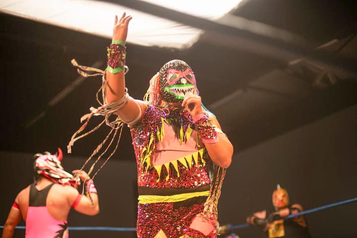 Colorful lucha libre wrestler in CDMX ring posing mid-match in a sparkling mask and costume.