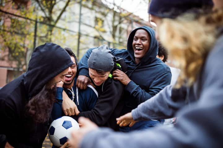 Des amis portant des sweats à capuche et équipés d'un ballon rient et se bousculent dans une rue à New York.