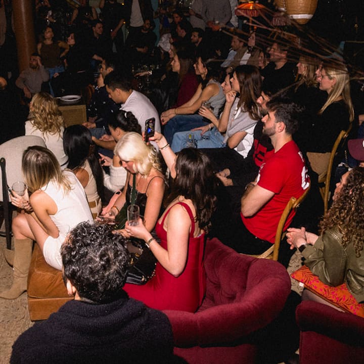 Un groupe de personnes, assises les unes à côté des autres lors d'un événement convivial à New York, assistent à une performance live ou à une expérience.