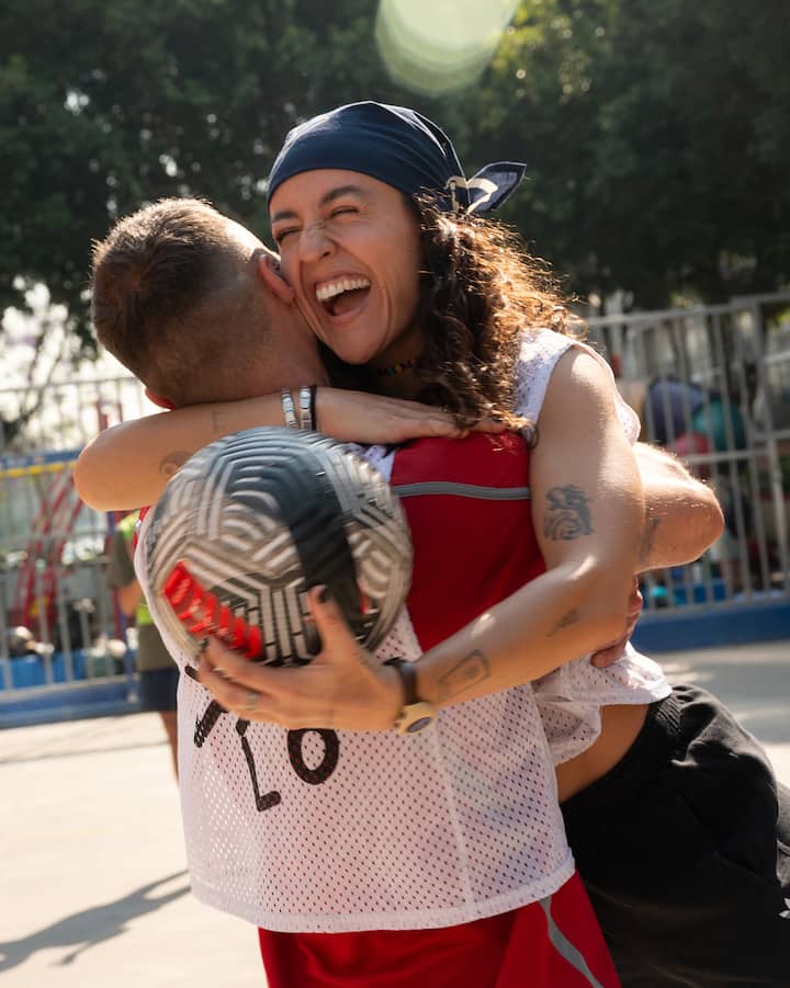 Fer Piña, souriante, tient un ballon de soccer en collant une autre joueuse de soccer.