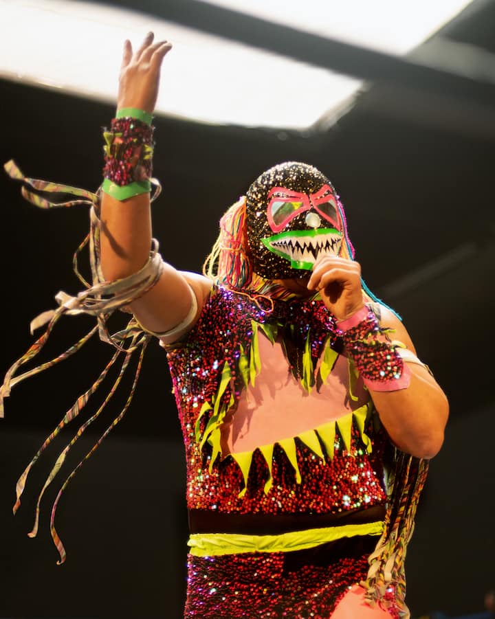 Un luchador haut en couleur prend une pose théâtrale en parlant depuis le ring.