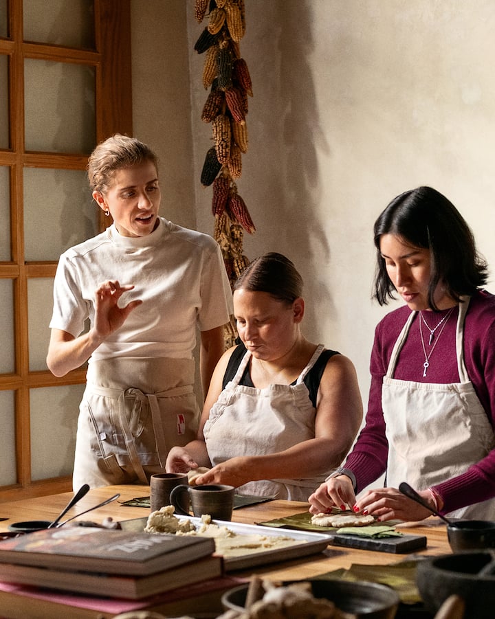 Une femme donne des instructions à deux autres femmes qui préparent des tamales sur une table.