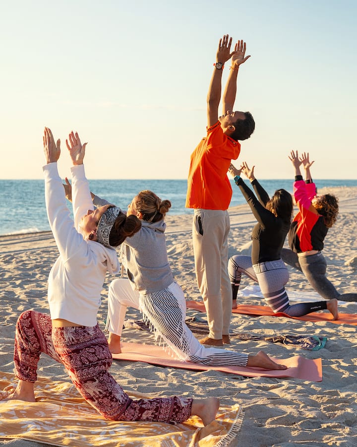 Six personnes font du yoga sur la plage au lever du soleil.