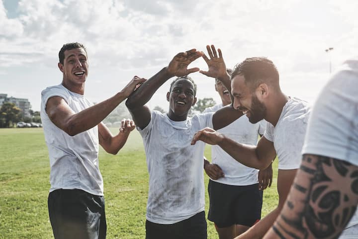 Soccer teammates in white jerseys celebrate together on a sunny field in Toronto during a match experience.