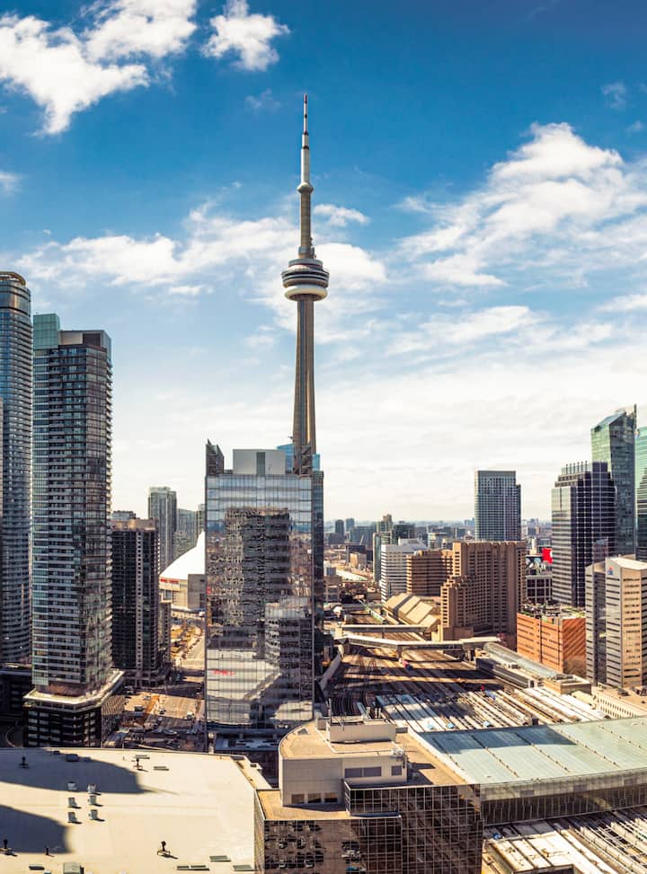 Daytime skyline with a tall observation tower rising above downtown high-rises and railway tracks. View more listings in Toronto..
