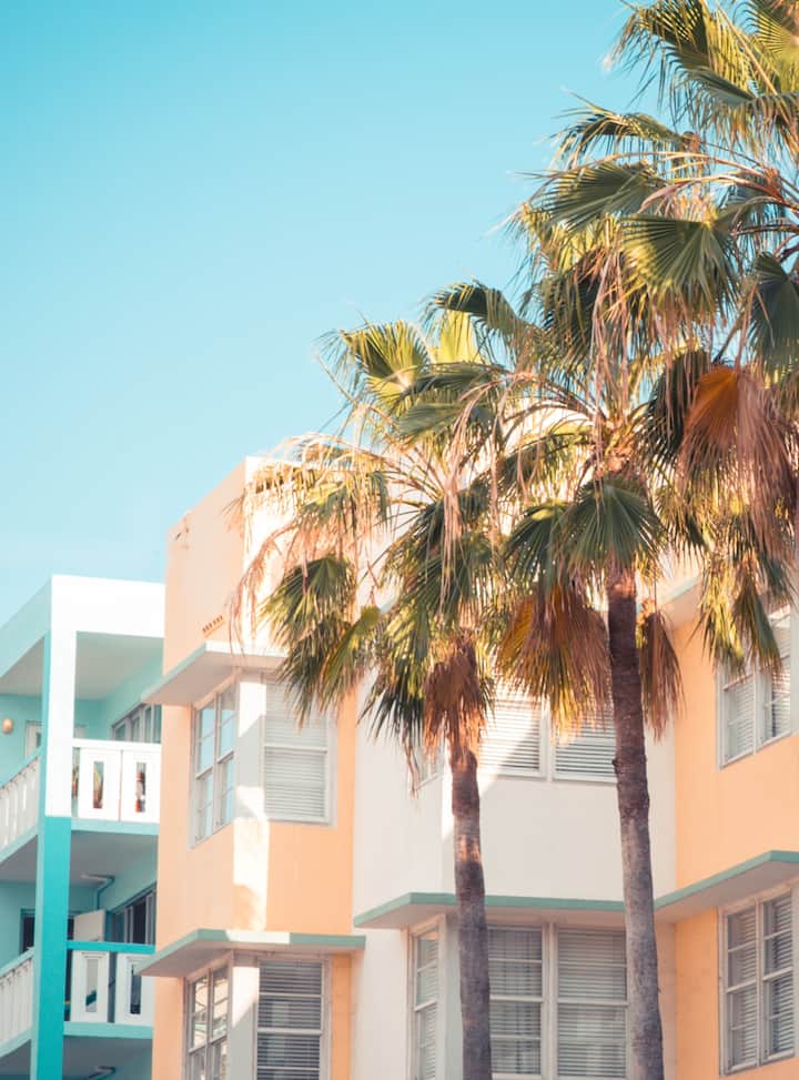 Pastel apartment building with tall palm trees against a clear blue sky. View more listings in Miami..