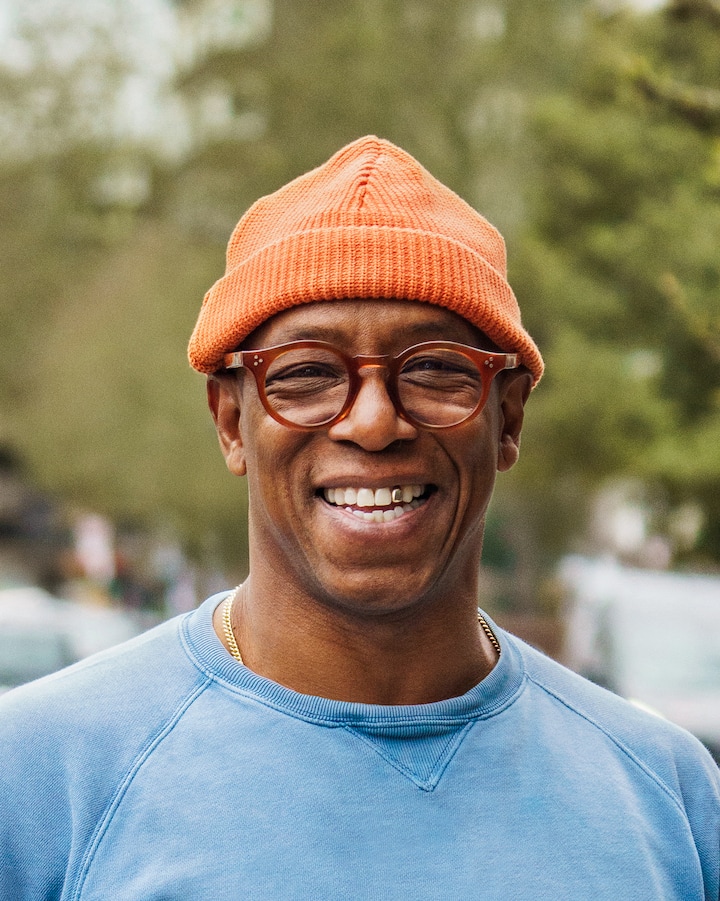 Ian Wright, vêtu d'un t-shirt bleu, fait un sourire à la caméra.