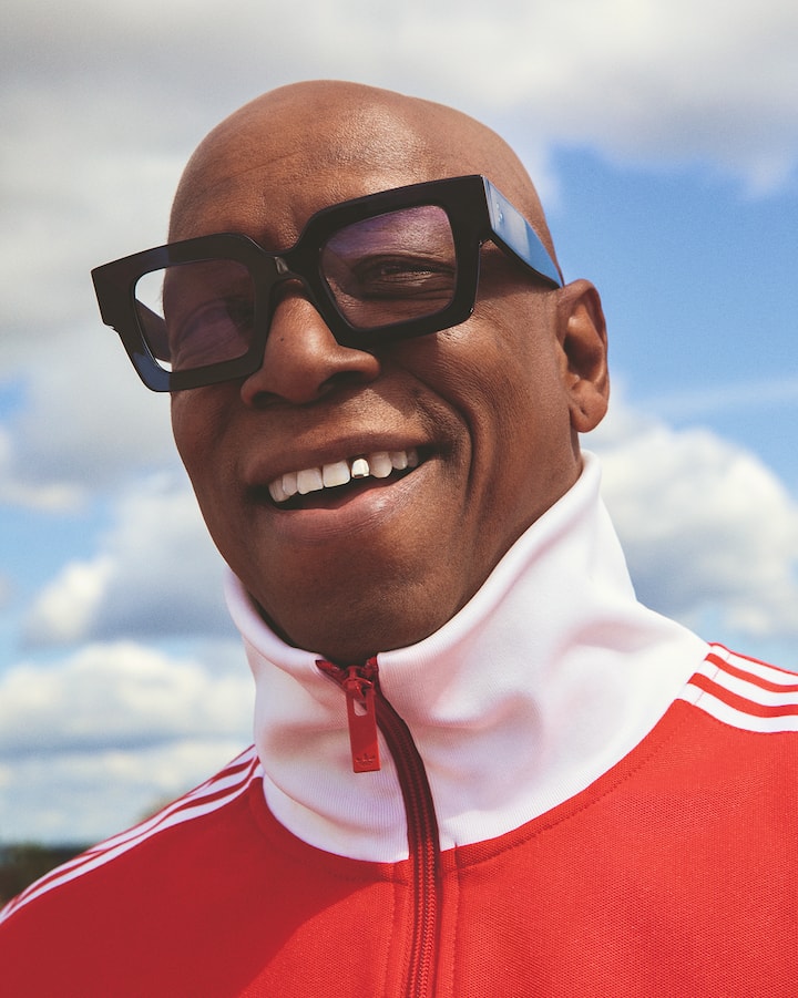 Ian Wright fait un sourire à la caméra en portant de grandes lunettes de soleil et un survêtement avec fermeture à glissière fermée.
