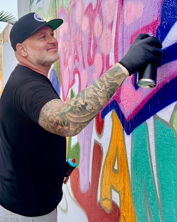 Un homme peint au pistolet une murale colorée.