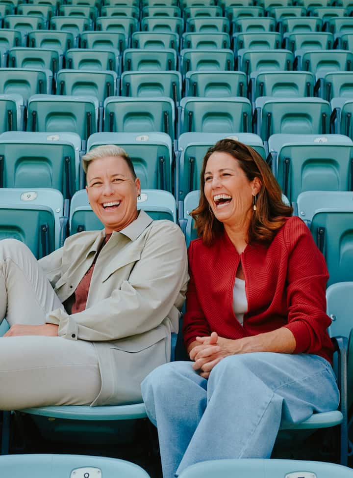 Friends sit together in teal stadium stands in LA, waiting for a FIFA game to start.